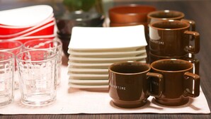 Una mesa con torres de platos blancos, vasos de vidrio transparentes y tazas marrones con la inscripción 'RELAX TIME'.