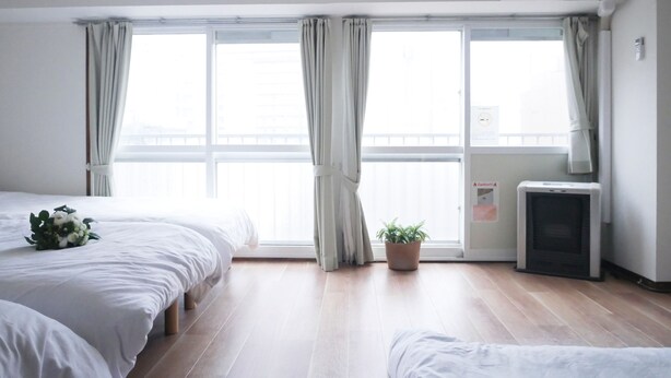 Habitación de hotel con dos camas, ventanas amplias, una planta en maceta, un equipo de aire acondicionado y un reloj en la pared.