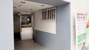 Entrada de un edificio con suelo de baldosas, una reja de metal y un cartel con texto en japonés.