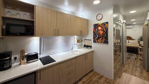 Une cuisine moderne avec des meubles en bois, un four à micro-ondes et un évier. Il y a un tableau au mur et une horloge au-dessus.