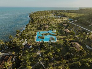 Vista aérea de un resort con piscina central, rodeado de palmeras y propiedades frente a la playa.