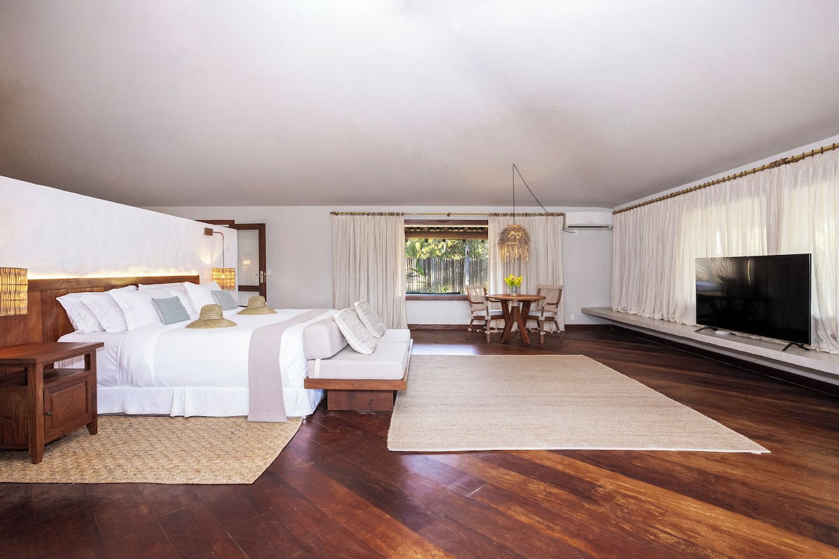 A spacious bedroom with a large bed, a TV, and a dining area with natural light.