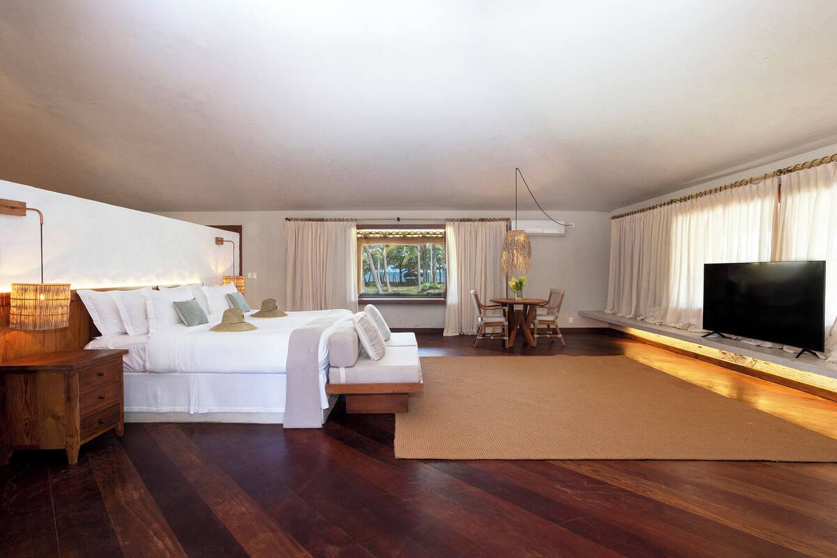 A bedroom with a bed, bedside table, TV, and a window with curtains.