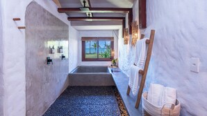 A narrow, stone-floored bathroom with a large bathtub, wooden beams, and a view of the ocean. - Reserva Jacumã Boutique Hotel  (Porto Seguro)