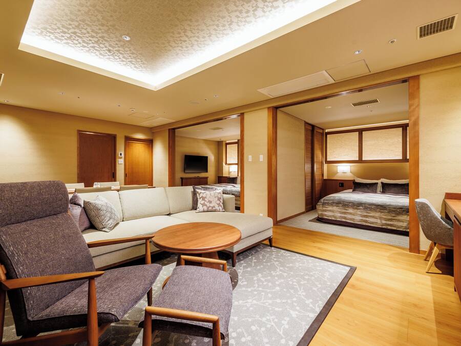 Habitación de hotel moderna con sofá, dos sillones, una mesita, cama y escritorio.