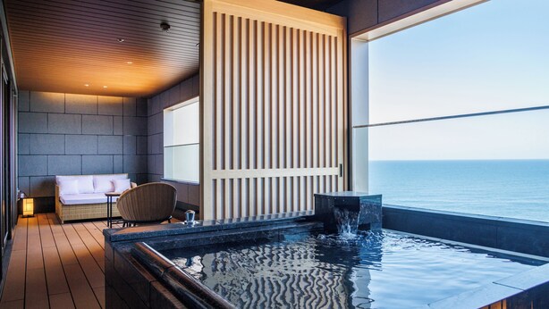 Zona d'una piscina interior moderna amb vista al mar, un espai d'estar amb sofà i cadires, i un paviment de fusta.
