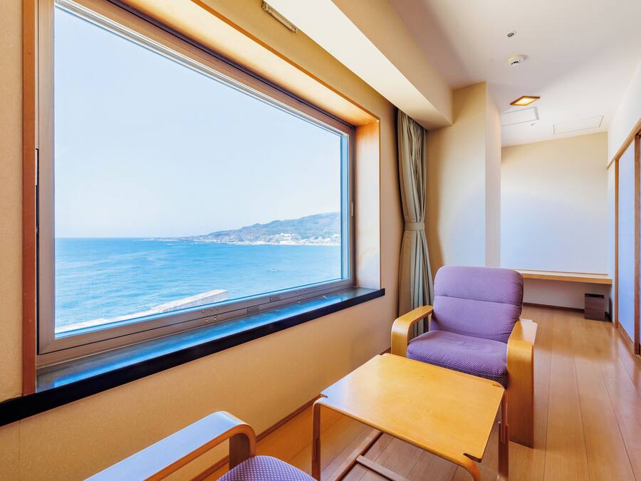 A cabin with a large window offering a view of the sea, a small table, and a purple chair.