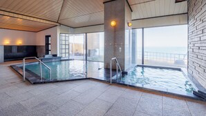 Una piscina interior moderna amb parets de vidre transparents, un sostre elevat i un pilaret de pedra.