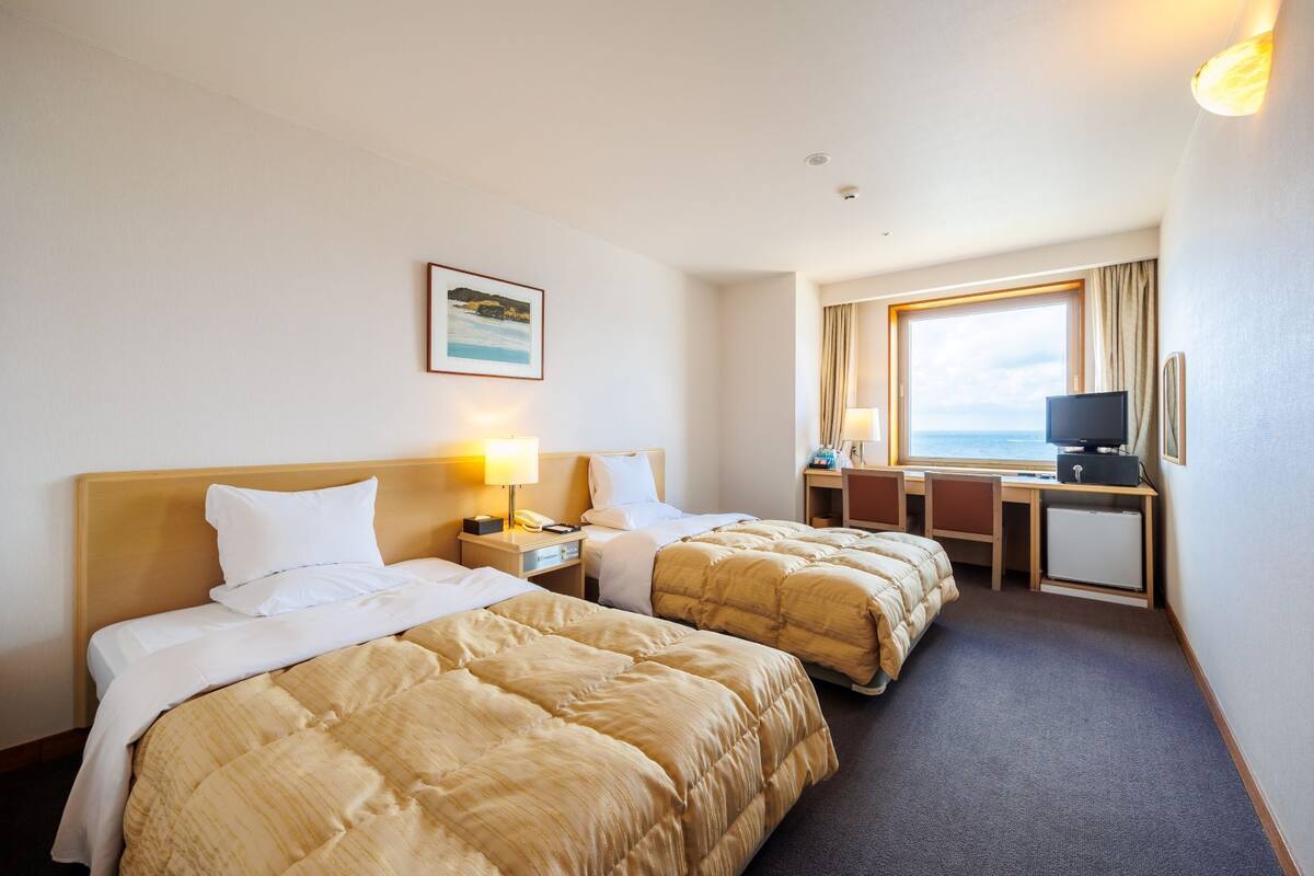 Une chambre d’hôtel avec deux lits, un bureau, une télévision et une fenêtre donnant sur la mer.