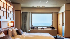 Habitació d'hotel amb un llit gran, zona de seients amb vista al mar i un mur amb panells de fusta.