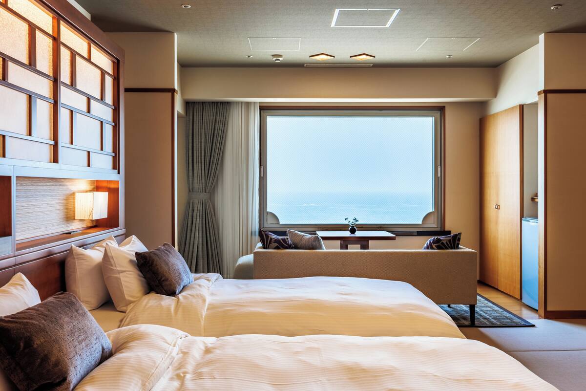 Une chambre d’hôtel avec un grand lit, un coin salon offrant une vue sur la mer et un mur revêtu de panneaux en bois.