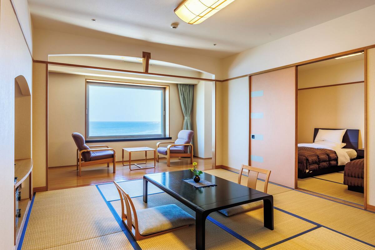 Une chambre d’hôtel avec une grande fenêtre, un lit, une table à manger et deux chaises.