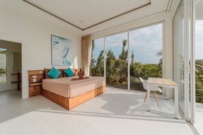 Ein modernes Schlafzimmer mit einem großen Bett, einem hölzernen Nachttisch, einem weißen Stuhl und Blick auf Bäume durch große Glasfenstertüren.