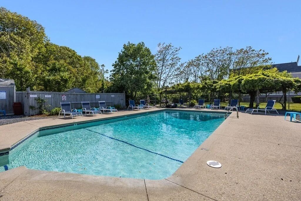 A rectangular swimming pool with clear blue water, surrounded by lounge chairs and a concrete deck.