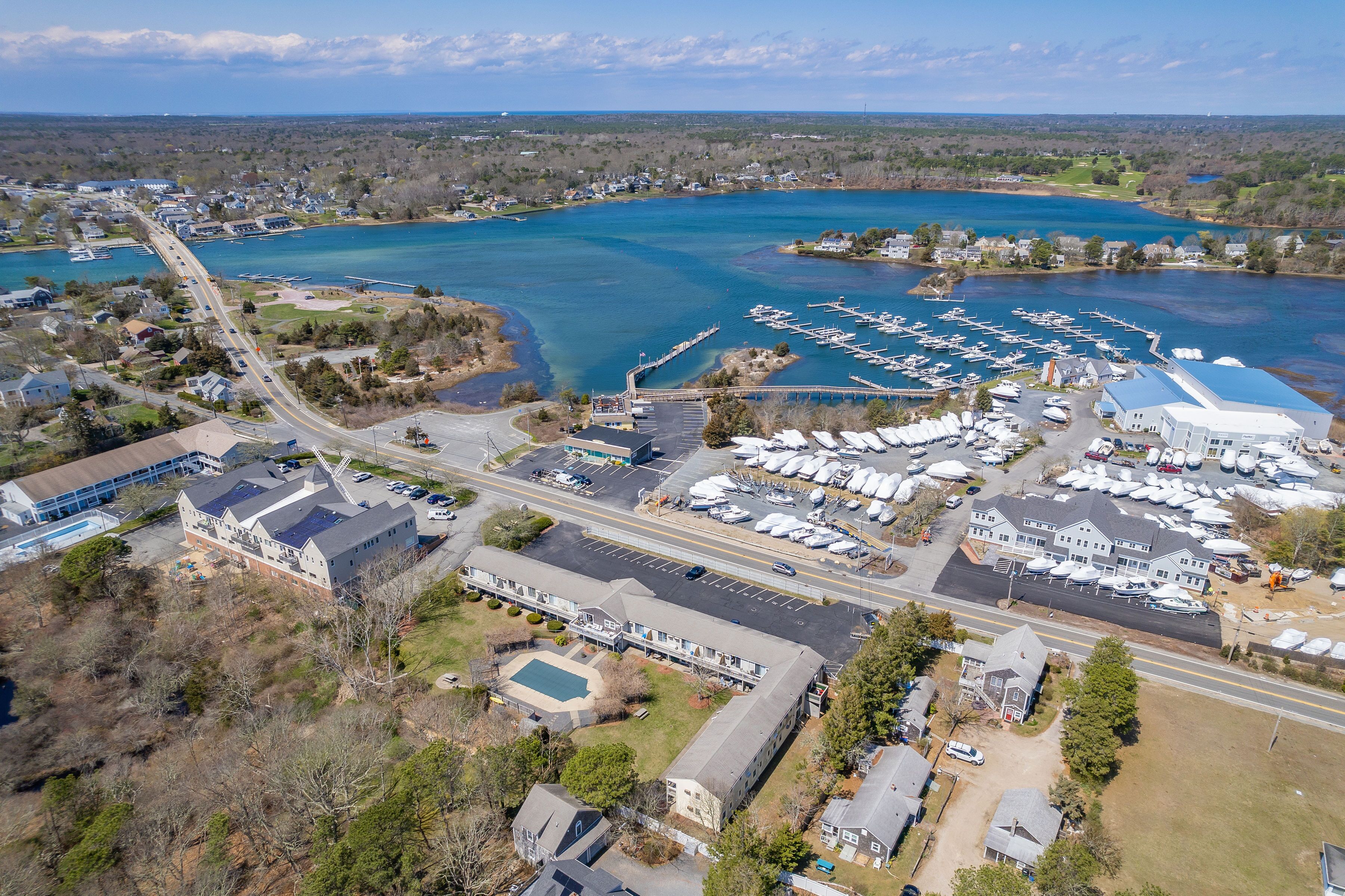 Une vue aérienne d’une marina où sont amarrés des bateaux, d’un grand bâtiment doté d’un toit bleu et d’une route qui longe les lieux.