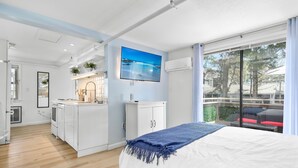 Una habitación de hotel moderna con una cama grande, una kitchenette pequeña, un televisor y un balcón con vistas al mar.
