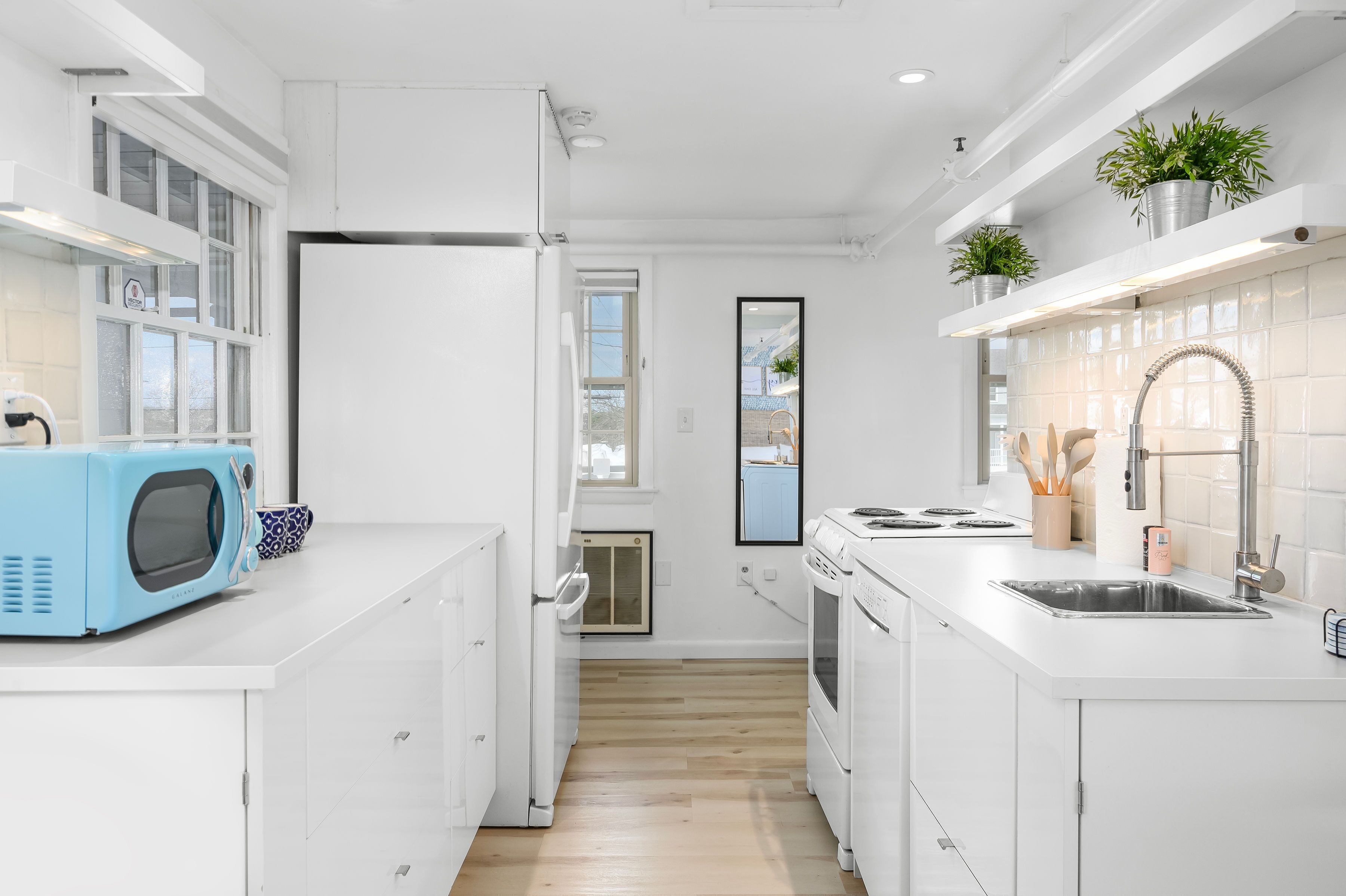 Une cuisine moderne avec des meubles blancs, un micro-ondes bleu, un évier en acier inoxydable et une fenêtre donnant sur la ville.