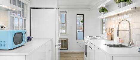 Une cuisine moderne avec des meubles blancs, un micro-ondes bleu, un évier en acier inoxydable et une fenêtre donnant sur la ville.