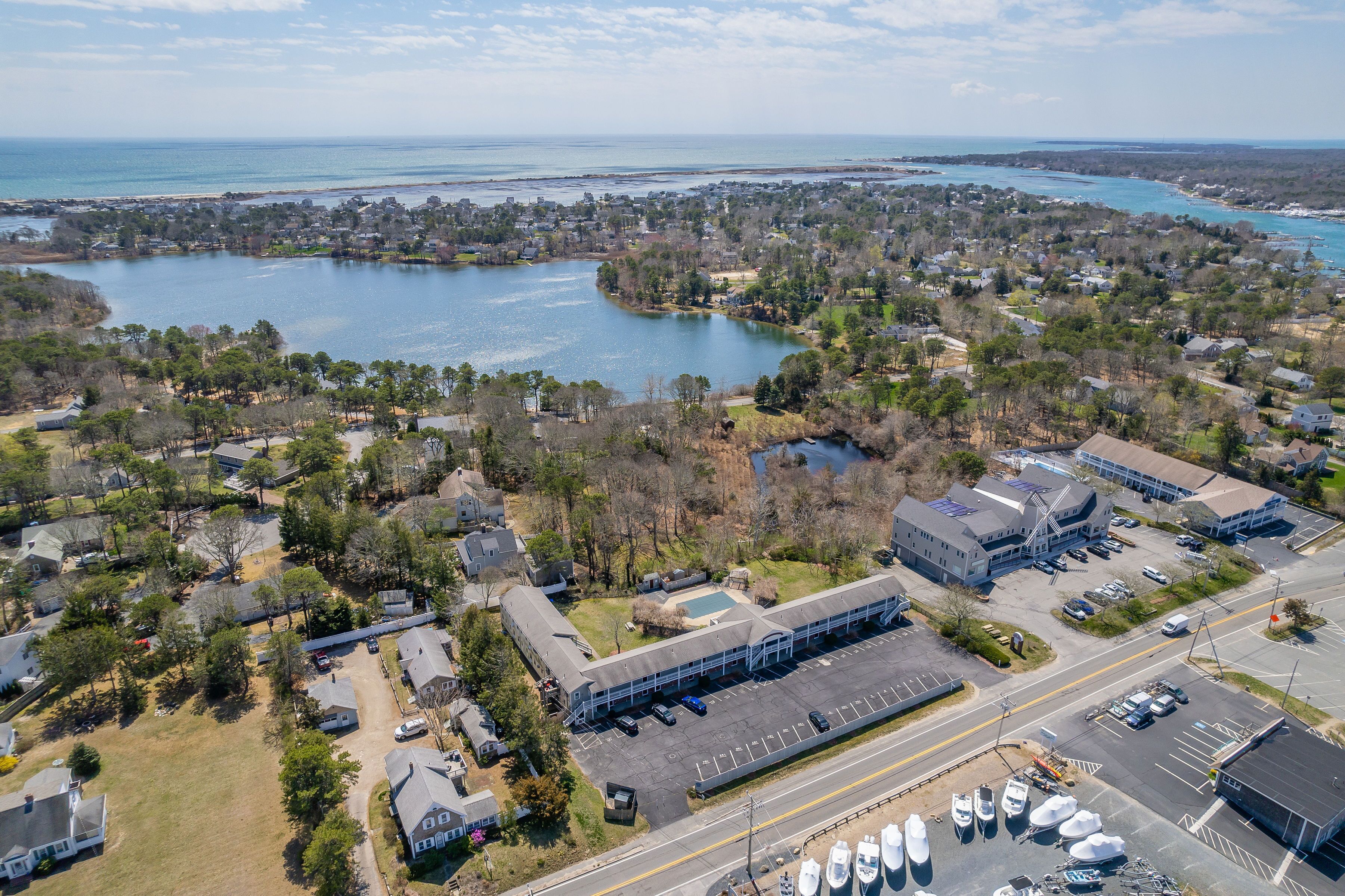 An aerial view of a coastal town with a marina, residential areas, and a large building with a parking lot.