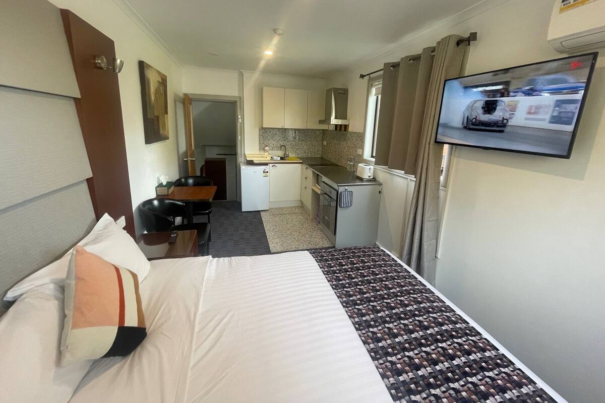 Une chambre d’hôtel compacte comprenant un lit, une petite kitchenette, un coin repas et un téléviseur fixé au mur.