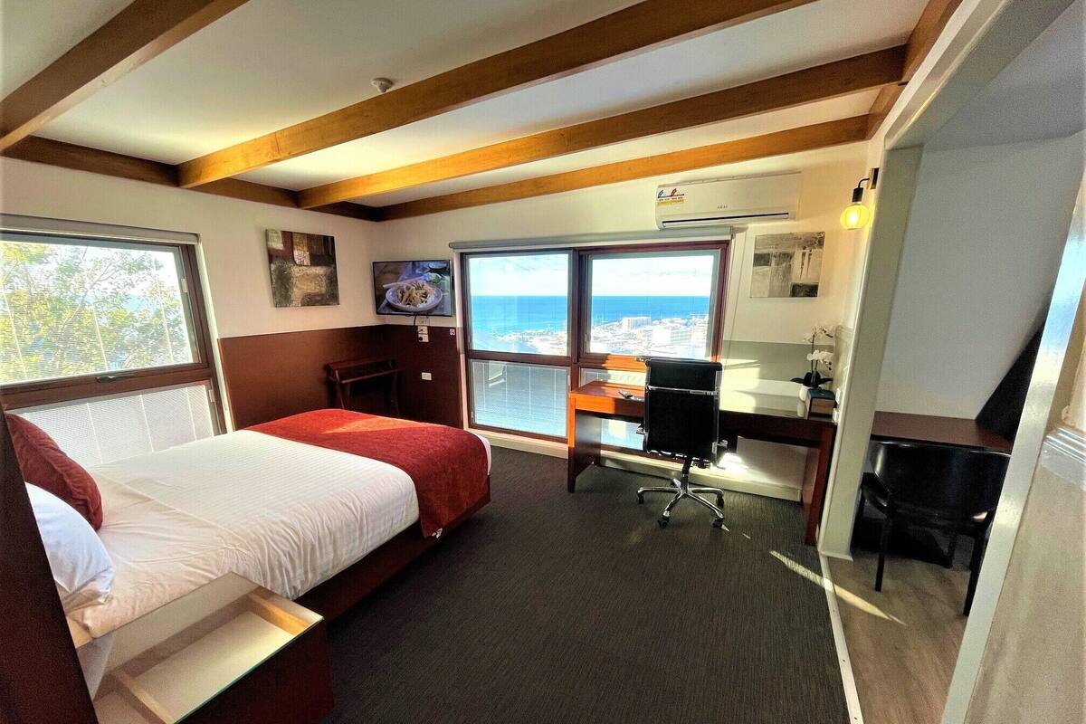 Une chambre d’hôtel avec deux lits, un bureau, une chaise, une télévision et une grande fenêtre donnant sur la ville.