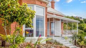 A house with a brick exterior, large windows, and a covered porch with white railings. - Oakleigh House (Burnie)
