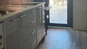A modern kitchen with a built-in stove, a sink, and a view of the sea through an open door. - Oakleigh House (Burnie)
