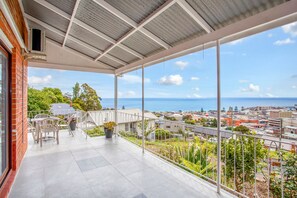 A balcony with a view of the sea and cityscape, featuring a table and chairs, and a potted plant. - Oakleigh House (Burnie)