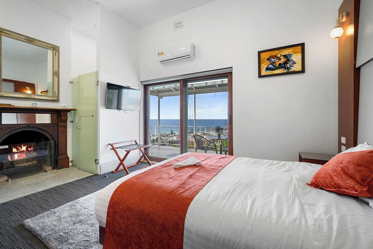 Une chambre d’hôtel avec un lit, une cheminée, un balcon avec vue et un téléviseur fixé au mur.
