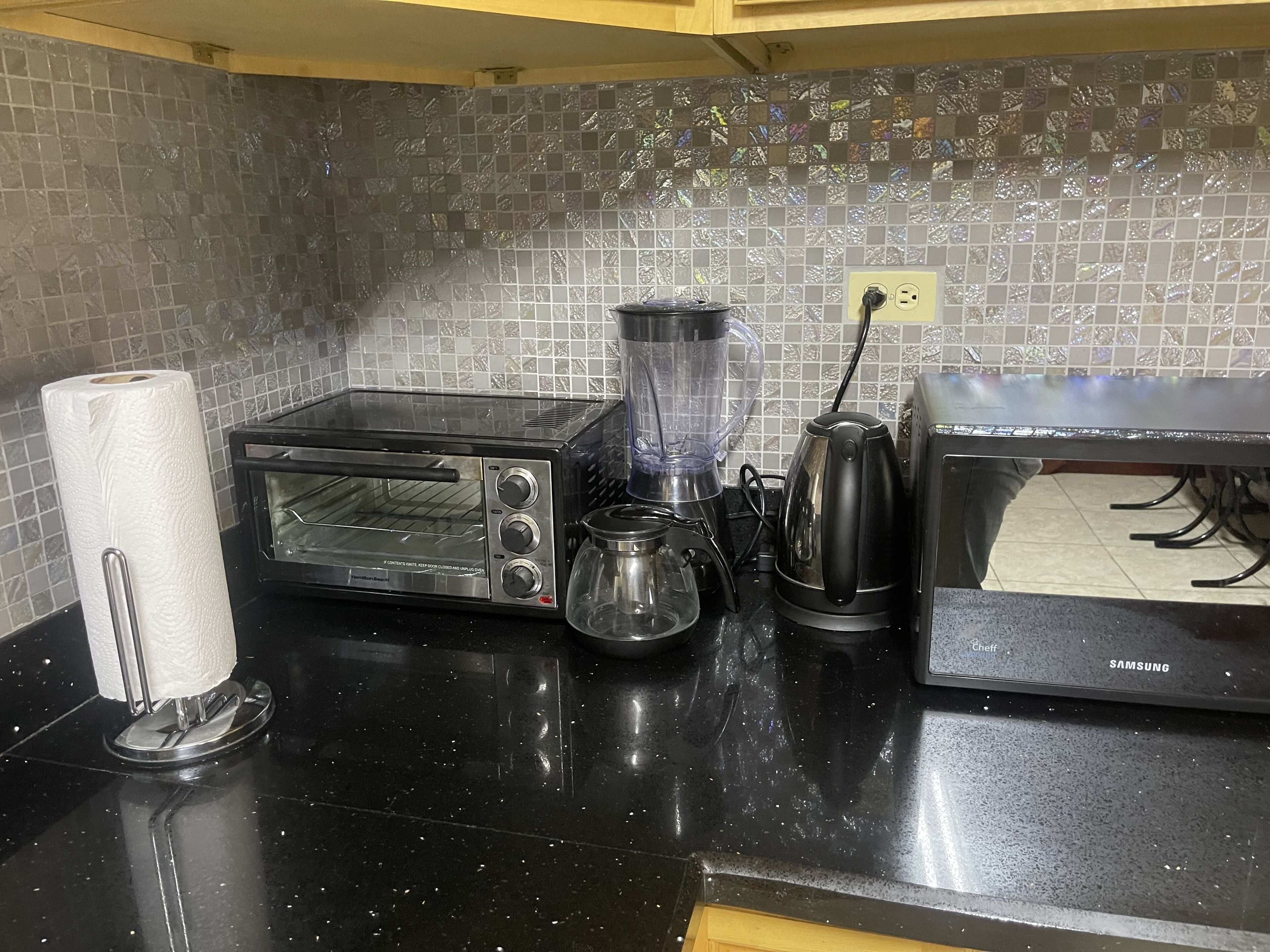 A kitchen with a toaster oven, a blender, a kettle, and a paper towel holder.
