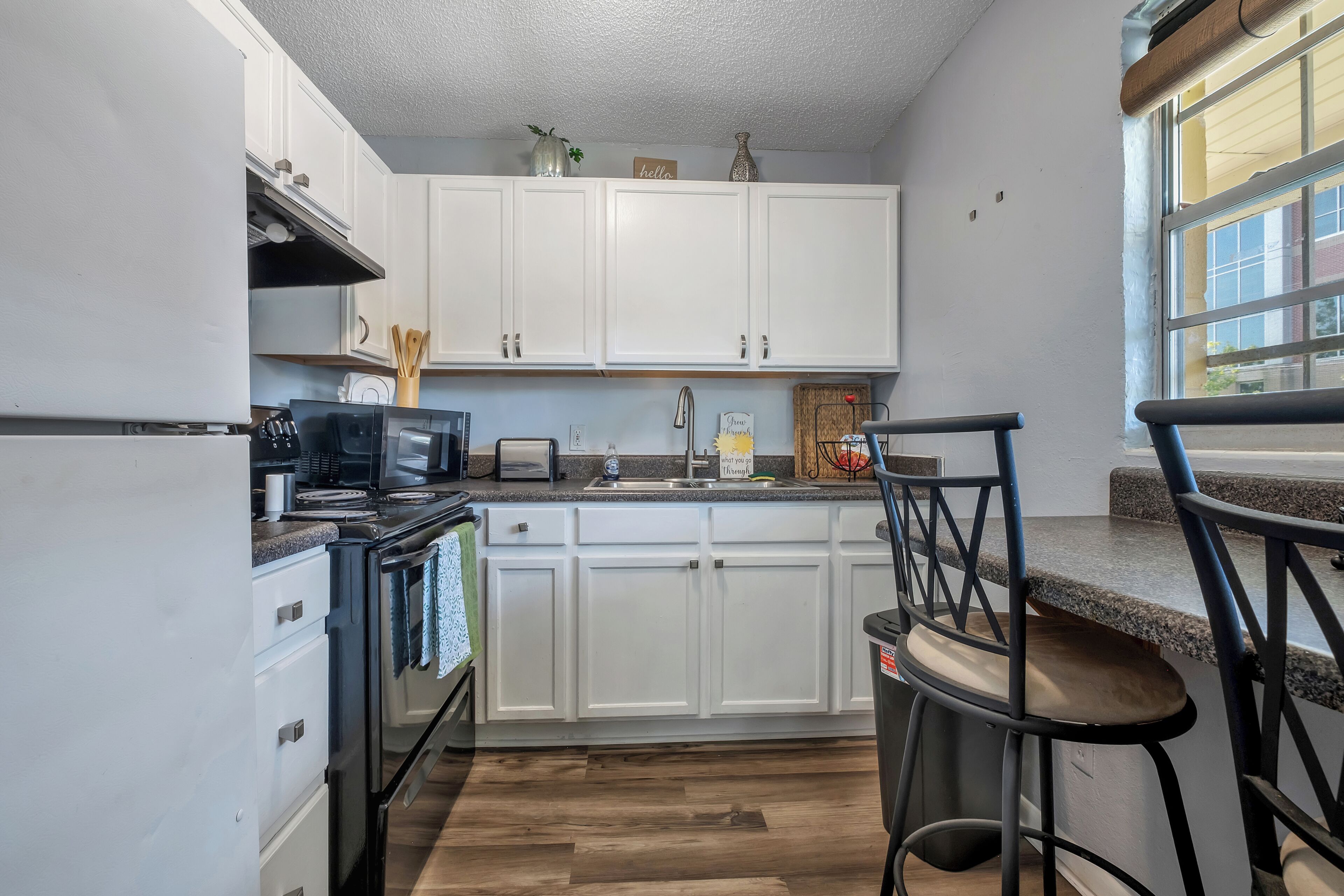 A kitchen with white cabinets, a black stove, a sink, and a bar stool.