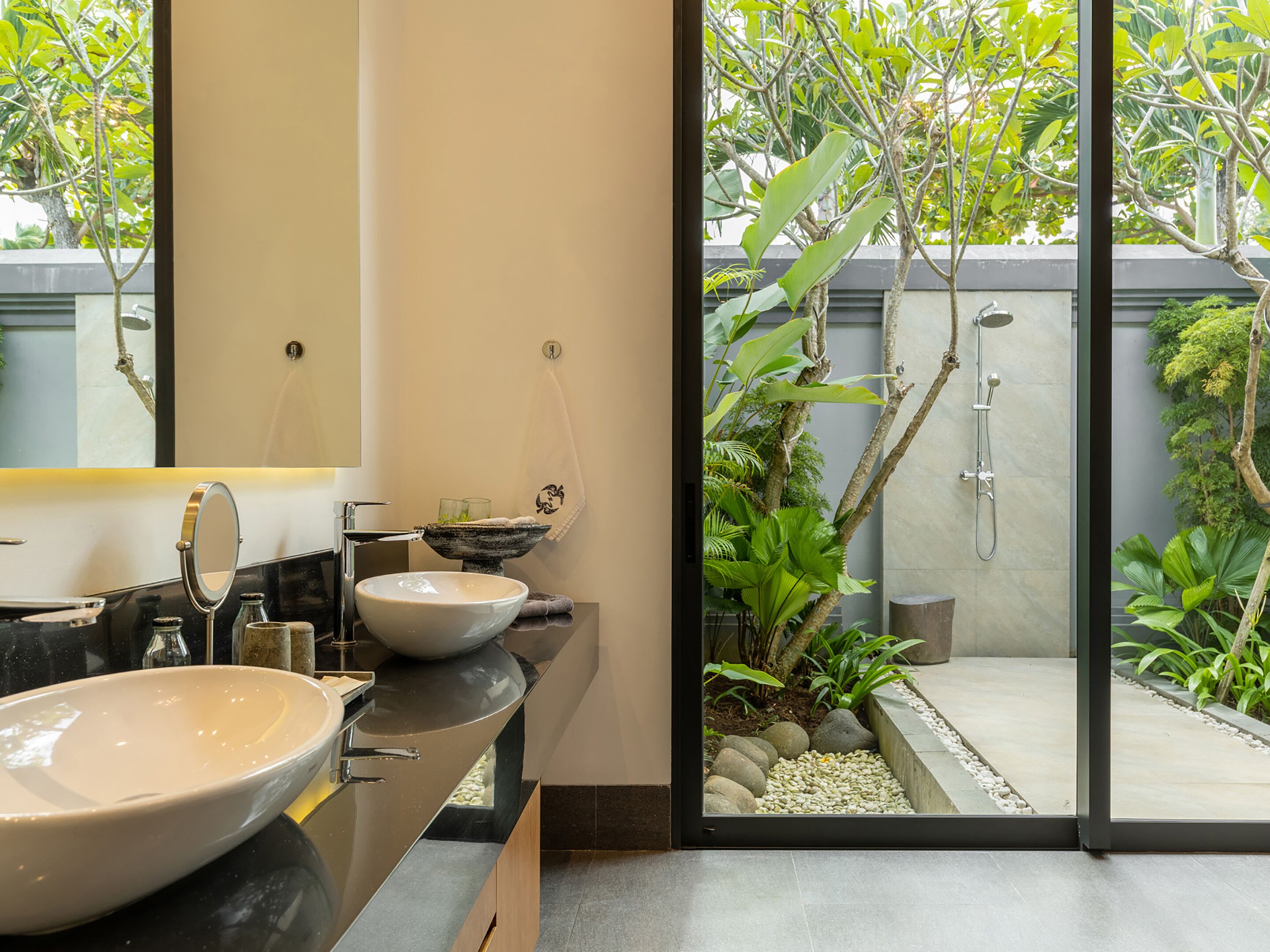 A modern bathroom with a large mirror, two sinks, and a shower area visible through a glass door.