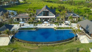Un moderno complejo turístico con una amplia piscina, mobiliario exterior y exuberante vegetación.