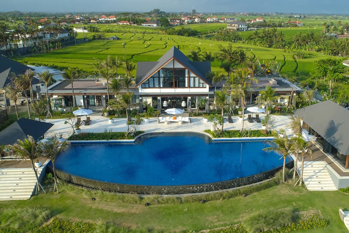 A modern resort with a large swimming pool, outdoor seating, and lush greenery.