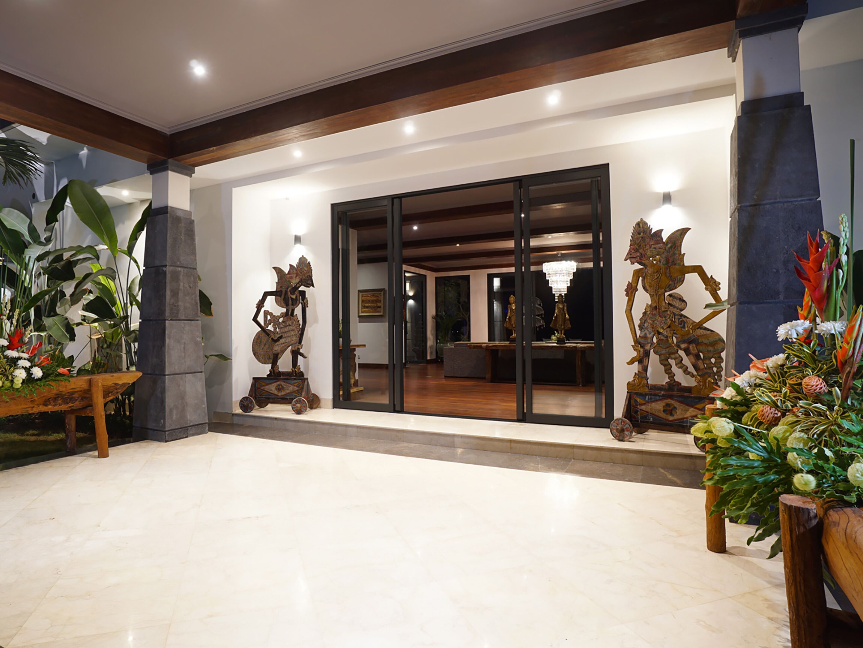 A lobby with a marble floor, wooden columns, and two large sculptures on pedestals.
