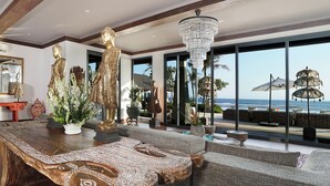 Amplia sala de estar con una gran mesa de madera, un candelabro y vista al océano.