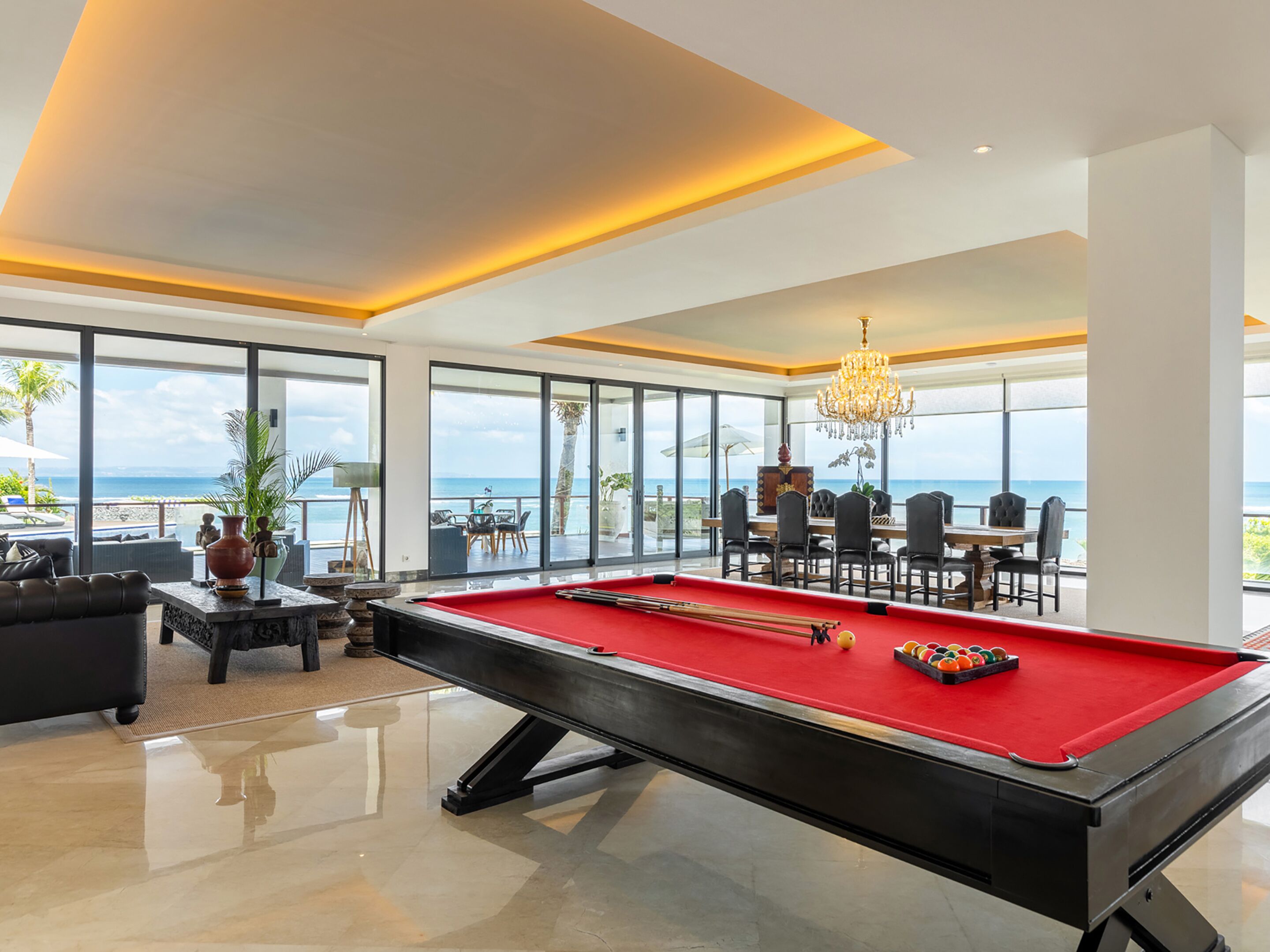 Un vaste espace piscine agrémenté d’une table de billard rouge, de sièges confortables et de grandes fenêtres offrant une vue sur l’océan.