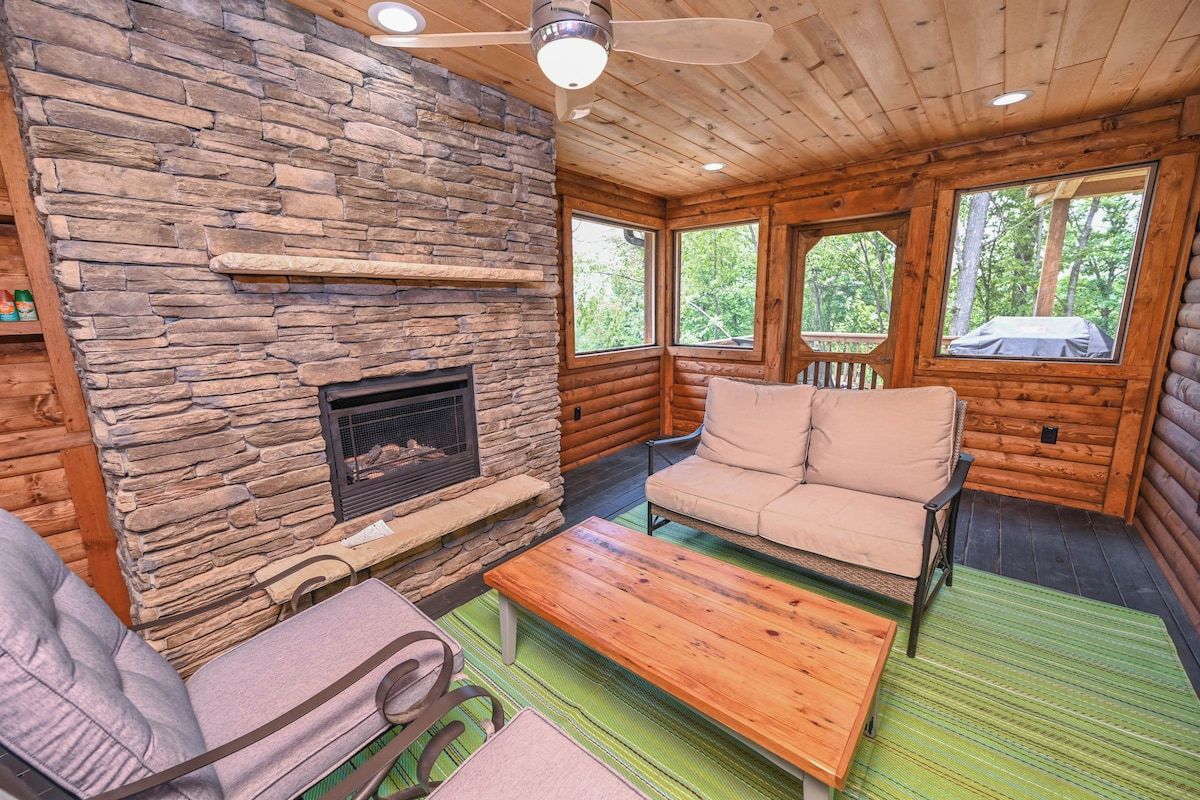 A log cabin interior with a stone fireplace, a sofa, and a ceiling fan.