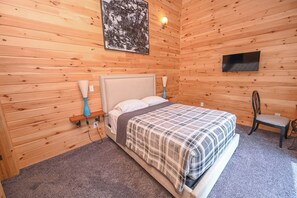 Une pièce aux murs lambrissés, comprenant un lit, un téléviseur et une chaise.