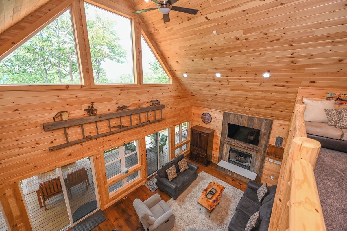 A wooden cabin interior with a loft bedroom, a fireplace, and a dining area.
