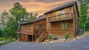 A two-story log cabin with a balcony on the upper floor, surrounded by trees. - Top-of-Wisp*6bed/6ba*Hottub* (McHenry)