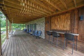 Un espace extérieur abrité doté d’une terrasse en bois, d’un mur en pierre et d’un bar avec des sièges.