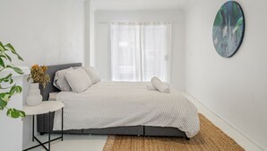 A bedroom with a bed, a bedside table, a vase with flowers, and a large abstract painting on the wall. - Oasis Lennox Head unit (Lennox Head)