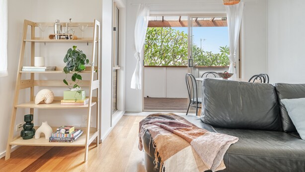 A modern living room with a sofa, a wooden bookshelf, and a balcony with a view of greenery. - Oasis Lennox Head unit (Lennox Head)