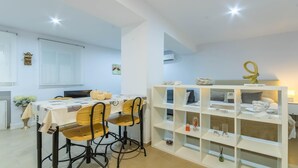 A modern, well-lit room with a dining table, chairs, and a white shelving unit with decorative items.