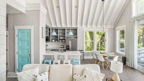 A modern kitchen with a central island, a dining area with a round table, and a living room with a sofa and chairs.