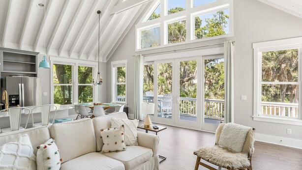 A spacious living area with a high ceiling, large windows, a kitchen, and a cozy seating area.