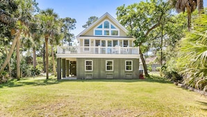 A two-story house with a balcony, surrounded by palm trees and a grassy yard.