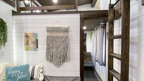 Una habitación acogedora con cama entrepiso, zona de estar con cojines, un macramé en la pared y una escalera de madera.