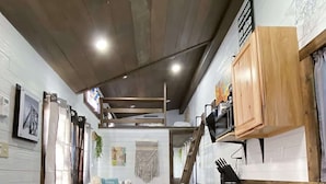 Una cocina compacta con armarios de madera, un refrigerador pequeño y una zona de comedor con un banco.